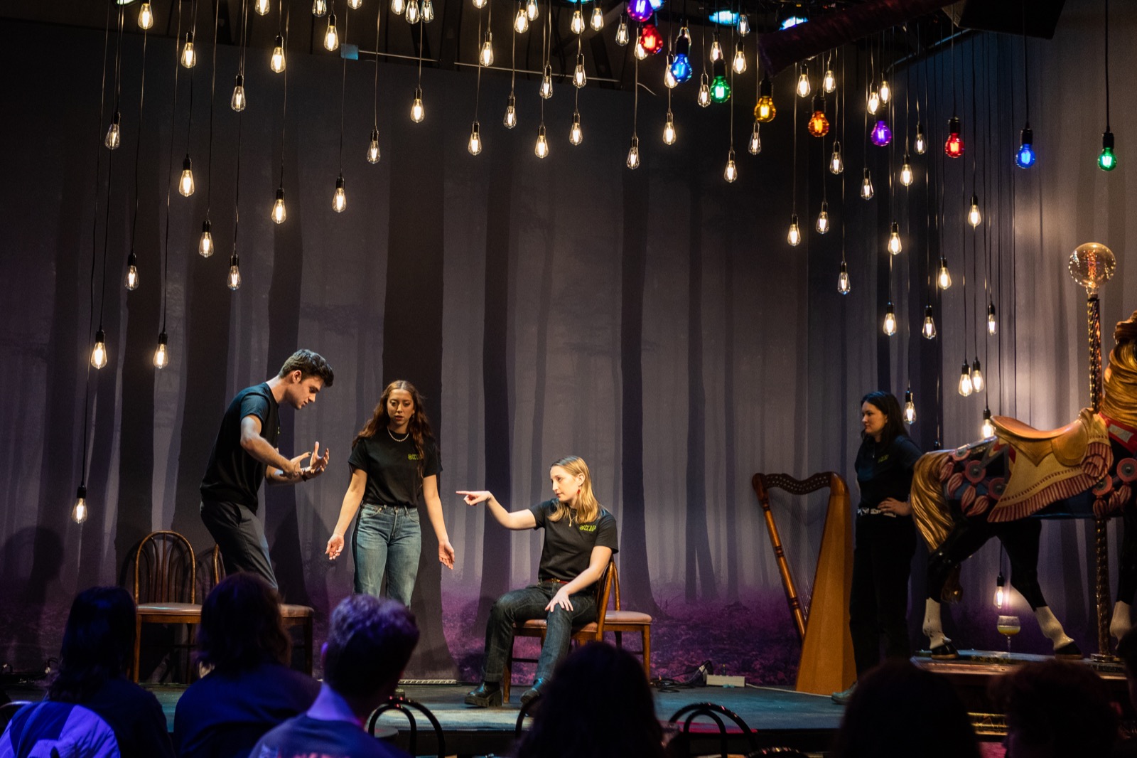 Skip Skip performing improv onstage on a forest-backdrop set, all four mid-scene with an audience watching